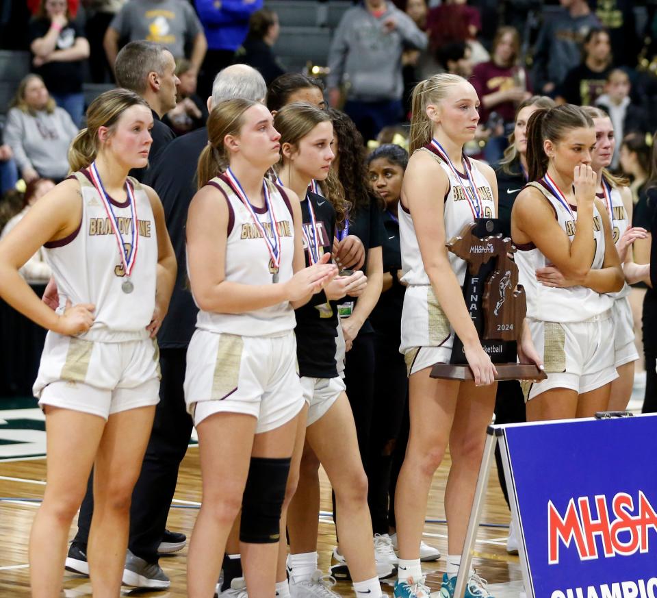 Brandywine players look on as senior Kadence Brumitt holds the state runner-up trophy following a 33-30 loss to Arbor Prep in the MHSAA Division 3 girls basketball state championship game Saturday, March 23, 2024, at the Breslin Center in East Lansing, Mich.