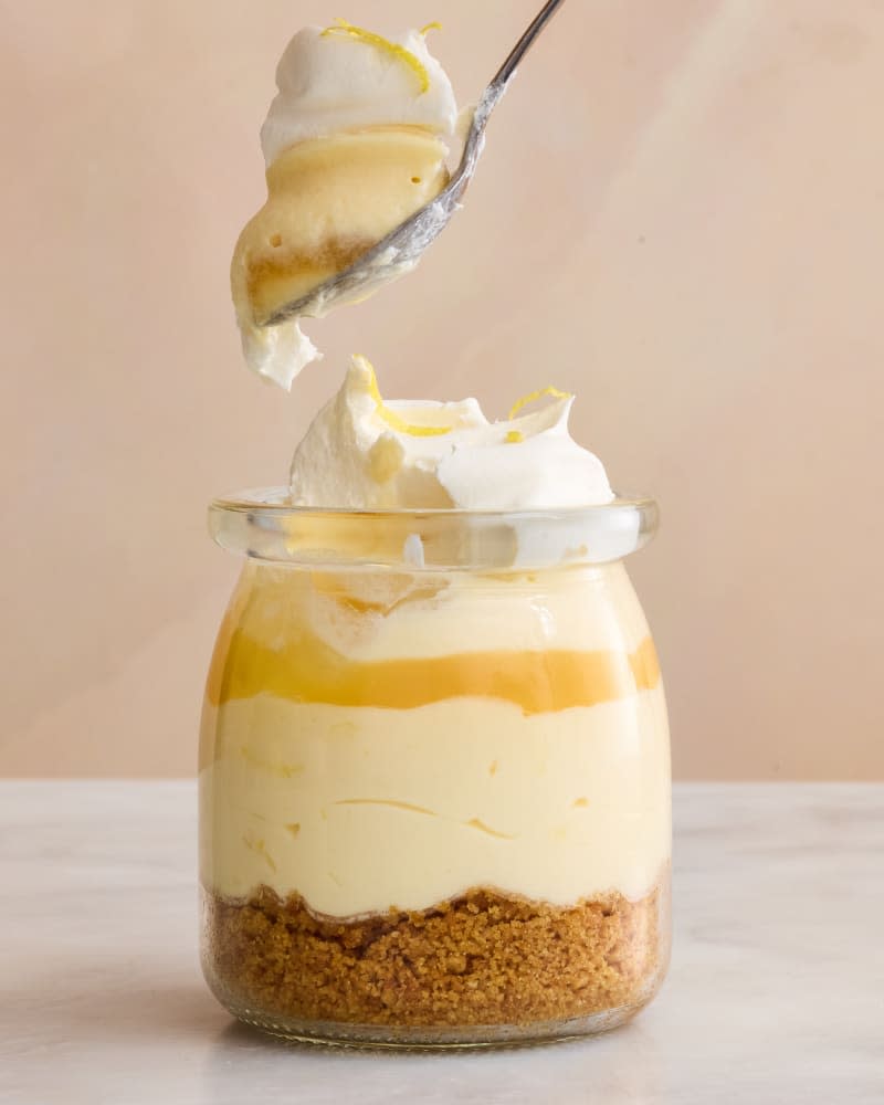 Head on shot of creamy lemon mousse in a small glass jar, with layers of graham cracker crumbs and whipped cream.