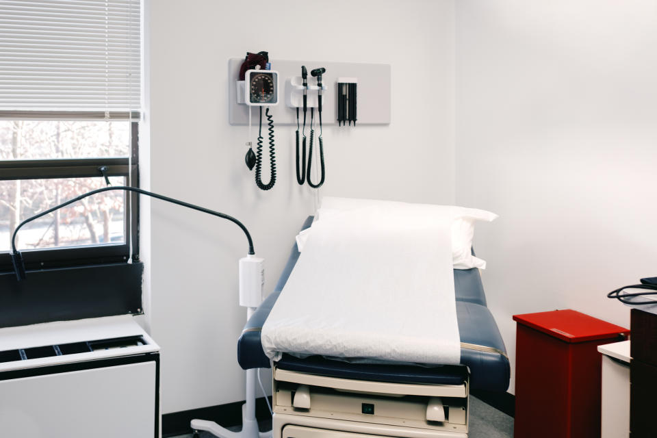 An empty medical examination room with an examination bed and medical equipment on the wall