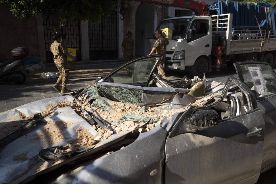 Lebanese army soldiers hold aid boxes past a destroyed car near the scene of last week's explosion that hit the seaport of Beirut, Lebanon, Wednesday, Aug. 12, 2020. (AP Photo/Hassan Ammar)