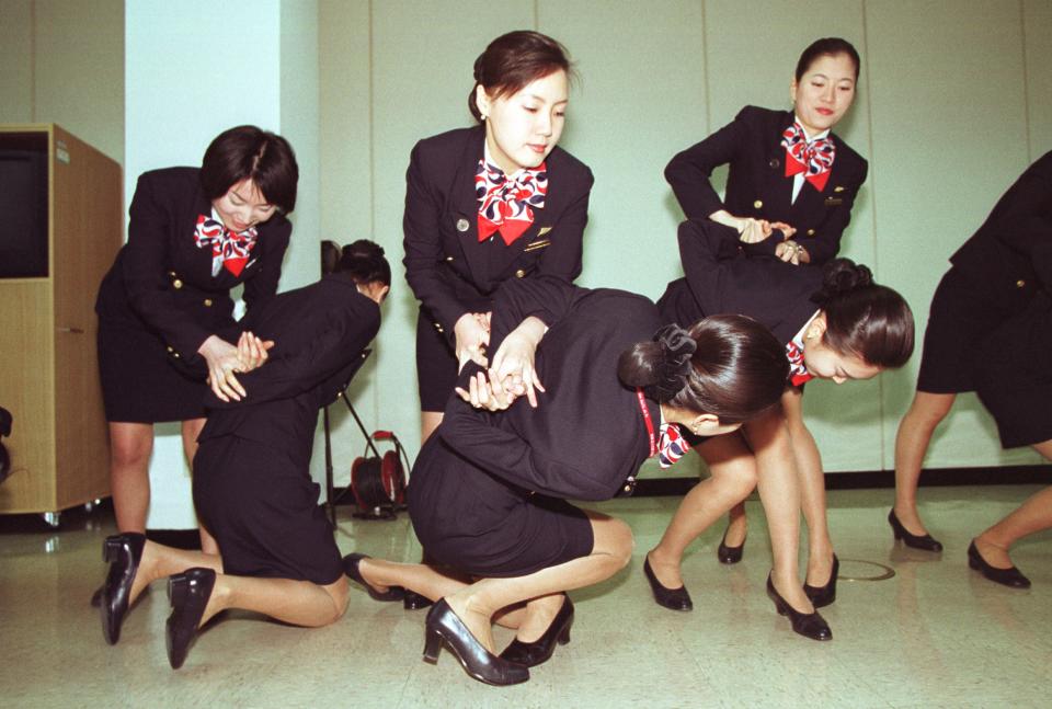 Three flight attendants restrain fellow flight attendants in a training drill.