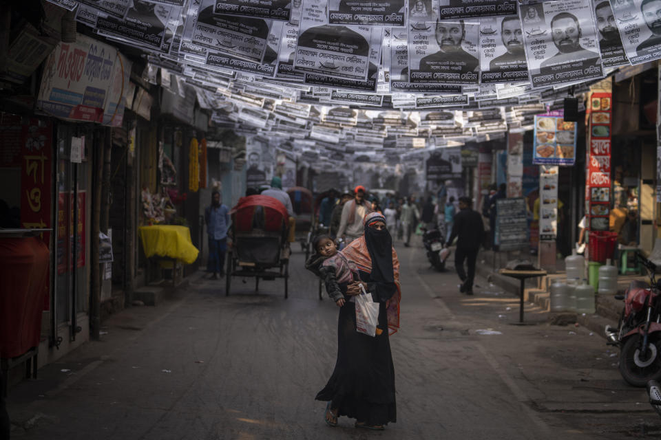 A woman walks with a child in her arms along a street with election campaign posters hanging in Dhaka, Bangladesh, Friday, Jan. 5, 2024. (AP Photo/Altaf Qadri)