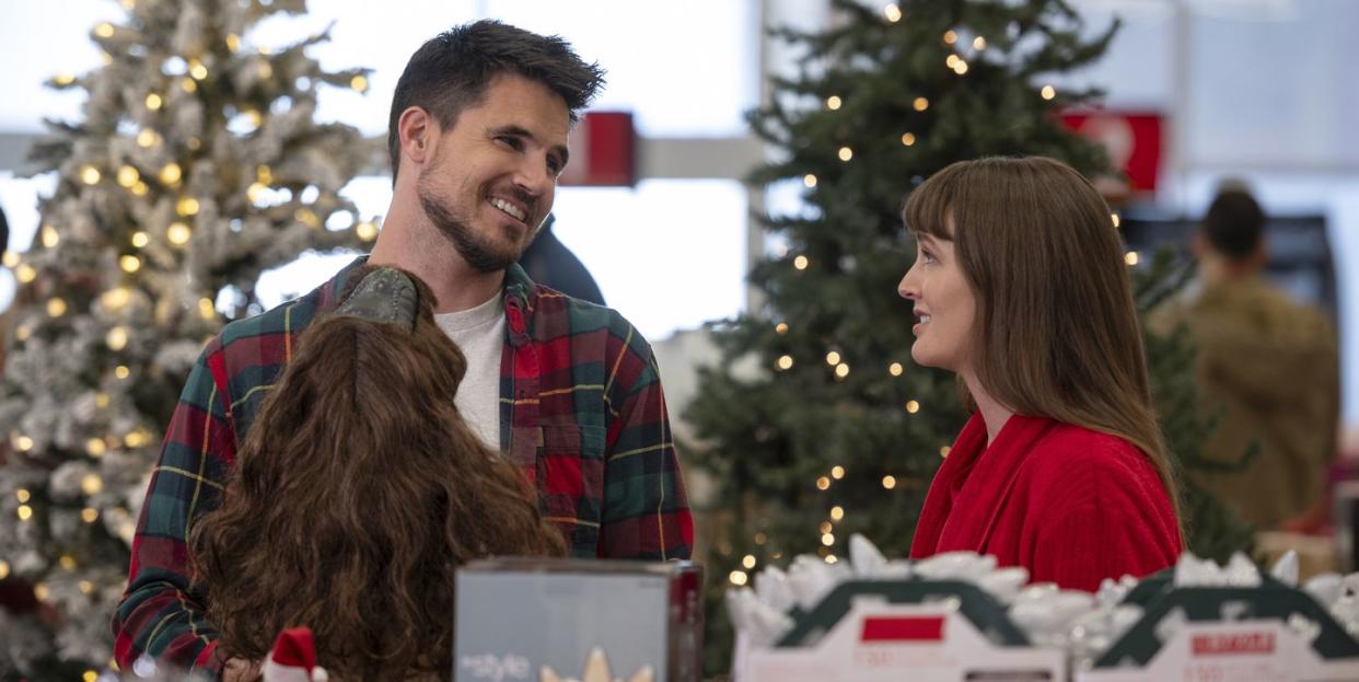 robbie amell and leighton meester star in exmas, a young couple stand in a shop surrounded by christmas decorations and smile at each other