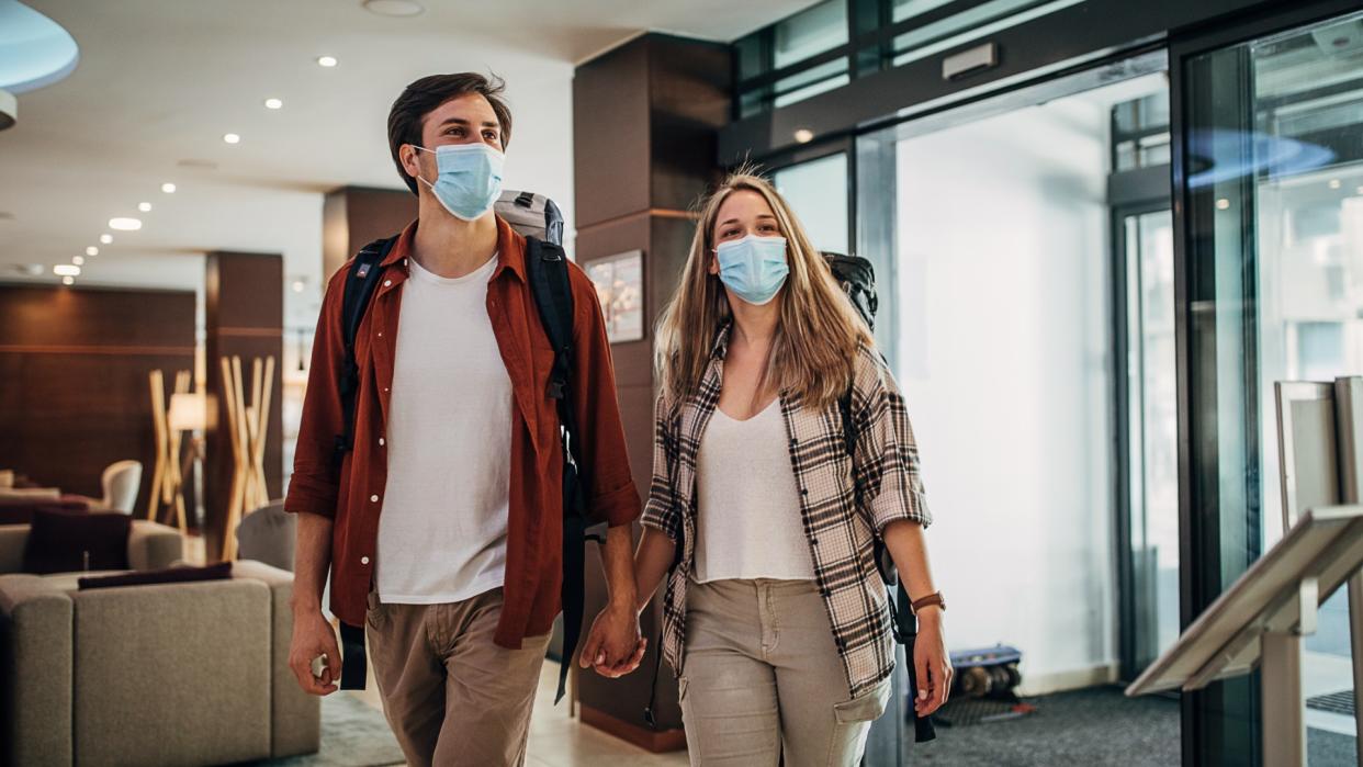 one-young-couple-with-protective-face-masks-entering-the-hotel-lobby-picture-id1252669989