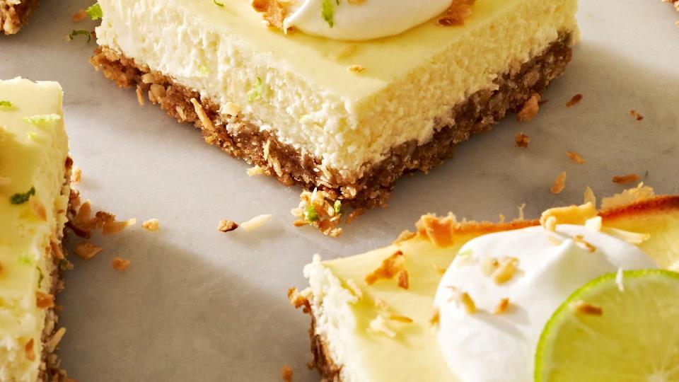 coconut key lime cheesecake bars with whipped cream, shredded toasted coconut, and lime