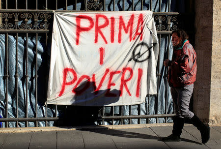 Angela Grossi walks past a banner reading "Poor first", hanging in a gate of the portico of the Basilica of the Santi Apostoli, where she lives after being evicted from an unused building along with other families in August 2017, in Rome, Italy January 29, 2018. Picture taken January 29, 2018. REUTERS/Tony Gentile