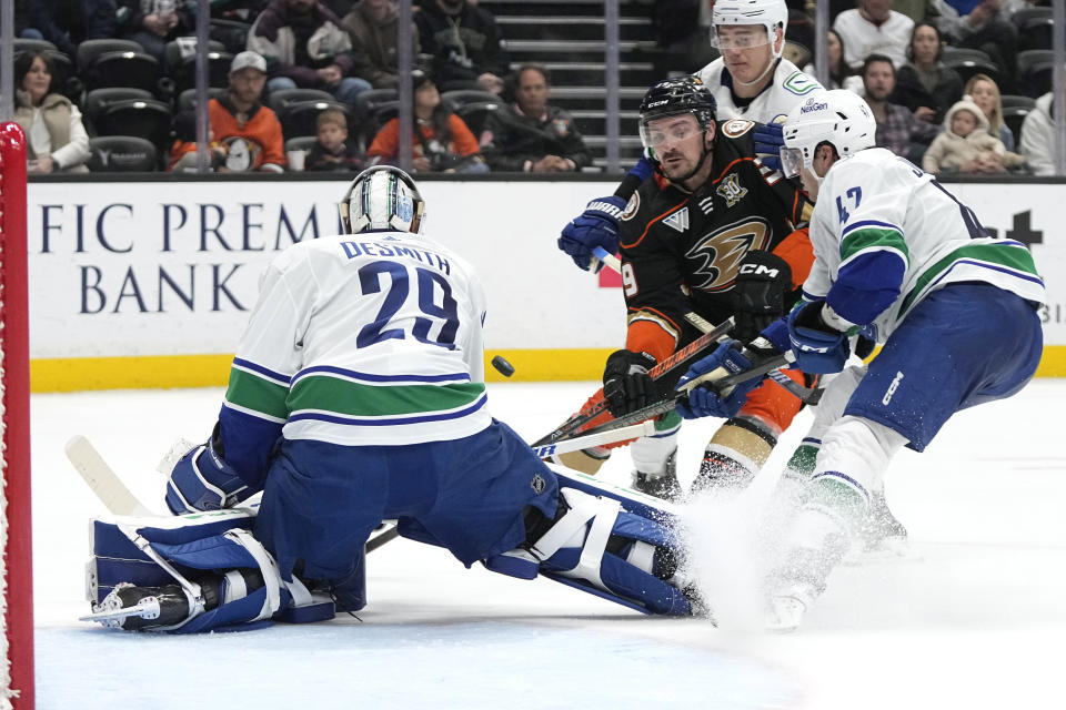 Anaheim Ducks center Sam Carrick, second from left, tries to score on Vancouver Canucks goaltender Casey DeSmith, left, as defenseman Noah Juulsen, right, defends during the third period of an NHL hockey game Sunday, March 3, 2024, in Anaheim, Calif. (AP Photo/Mark J. Terrill)