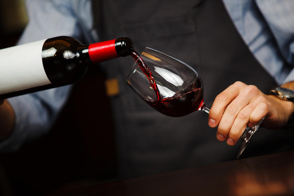 Man pouring wine into wineglass, male hand holding bottle of red expensive alchoholic beverage, closeup photo
