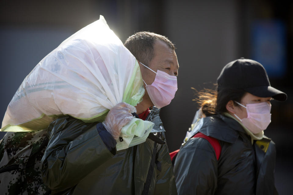 Travelers wear face masks as they walk outside the Beijing Railway Station in Beijing, Saturday, Feb. 15, 2020. People returning to Beijing will now have to isolate themselves either at home or in a concentrated area for medical observation, said a notice from the Chinese capital's prevention and control work group published by state media late Friday. (AP Photo/Mark Schiefelbein)