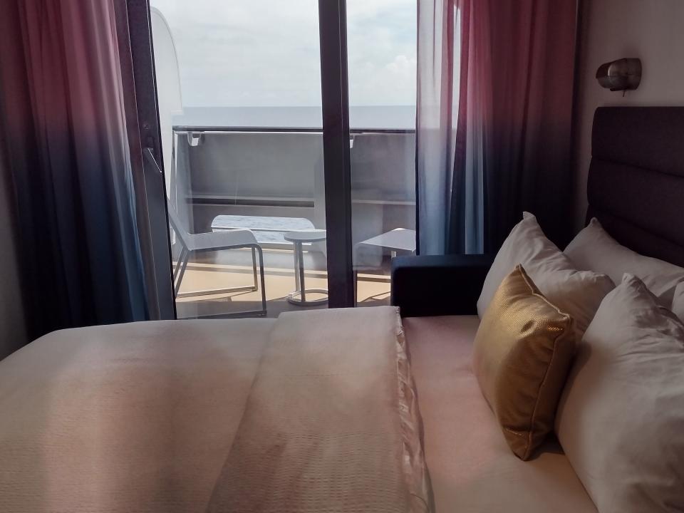 A cruise ship bed with curtains open to show the balcony.