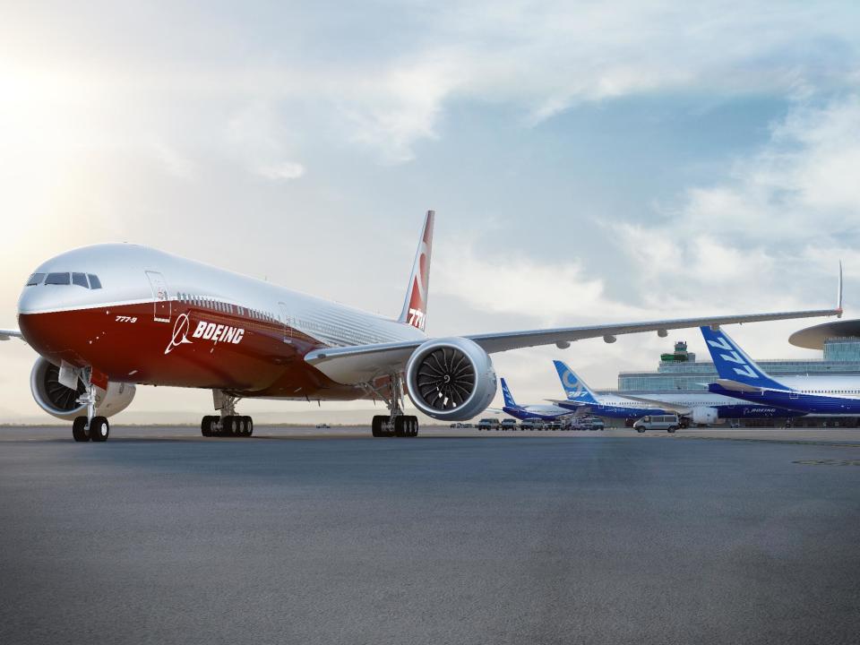 One red plane with the Boeing logo on the airport ramp and several planes with blue tails in the background.