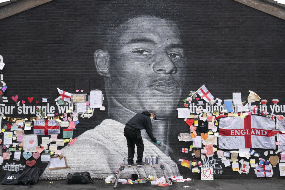 Street artist Akse P19 repairs the mural of Manchester United striker and England player Marcus Rashford on the wall of the Coffee House Cafe on Copson Street, in Withington, Manchester, England, Tuesday July 13, 2021. The mural was defaced with graffiti in the wake of England losing the Euro 2020 soccer championship final match to Italy, but subsequently covered with messages of support by well wishers. (AP Photo/Jon Super)