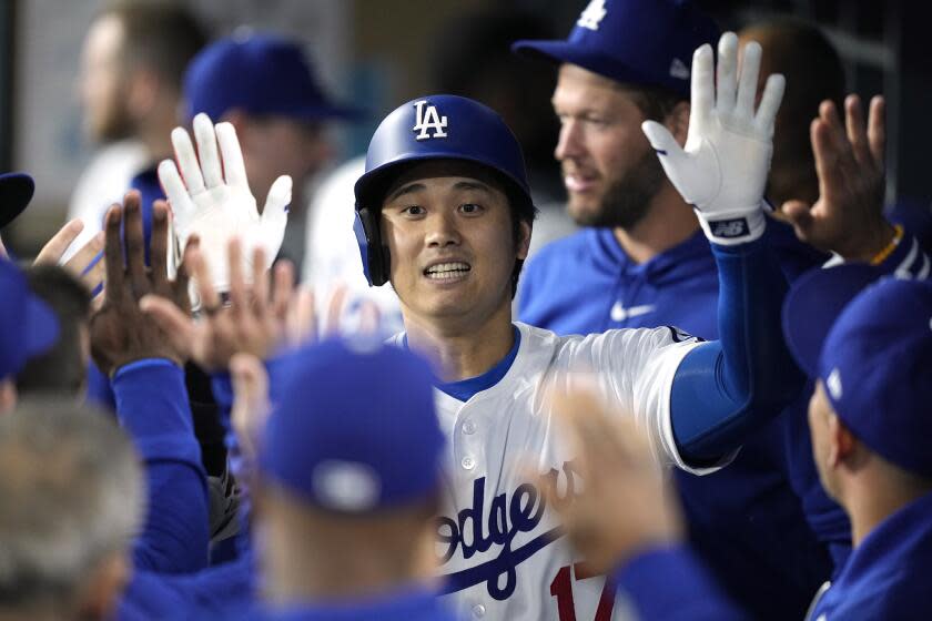 Los Angeles Dodgers' Shohei Ohtani is congratulated by teammates in the dugout.