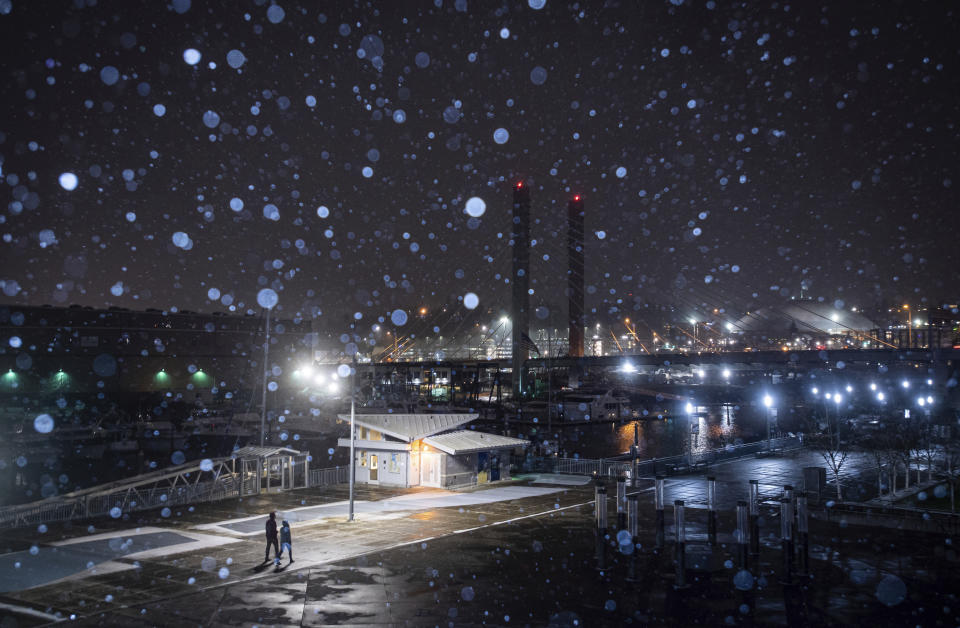 People walk along the Thea Foss Waterway as snow begins to fall in Tacoma, Wash., on Thursday, Feb. 11, 2021. A winter storm blanketed the Pacific Northwest with ice and snow Saturday, leaving hundreds of thousands of people without power and disrupting travel across the region. (Joshua Bessex/The News Tribune via AP)