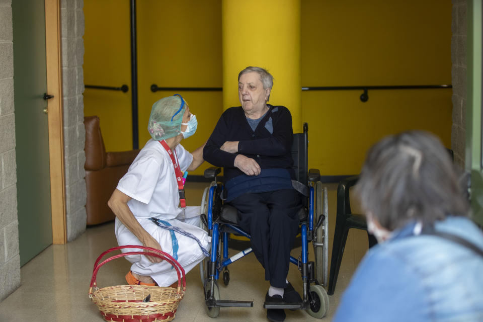 Maria Giulia Badaschi, health director, at the Martino Zanchi Foundation nursing home reassures Laura Ricardi, 86, as she sits in a wheelchair at a safe distance to talk to her family in Alzano Lombardo, Italy, Friday, May 29, 2020. Loved ones are being allowed to reunite with residents of the Martino Zanchi Foundation nursing home in the northern Italian town of Alzano. It comes after more than three months of separation and worry amid the coronavirus pandemic. Alzano, close to Bergamo, is the site of one of Italy's biggest outbreaks, centered around the town's hospital. (AP Photo/Luca Bruno)