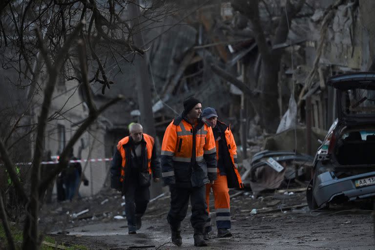 Trabajadores comunales caminan junto a casas residenciales que fueron parcialmente destruidas por un bombardeo ruso en la capital ucraniana