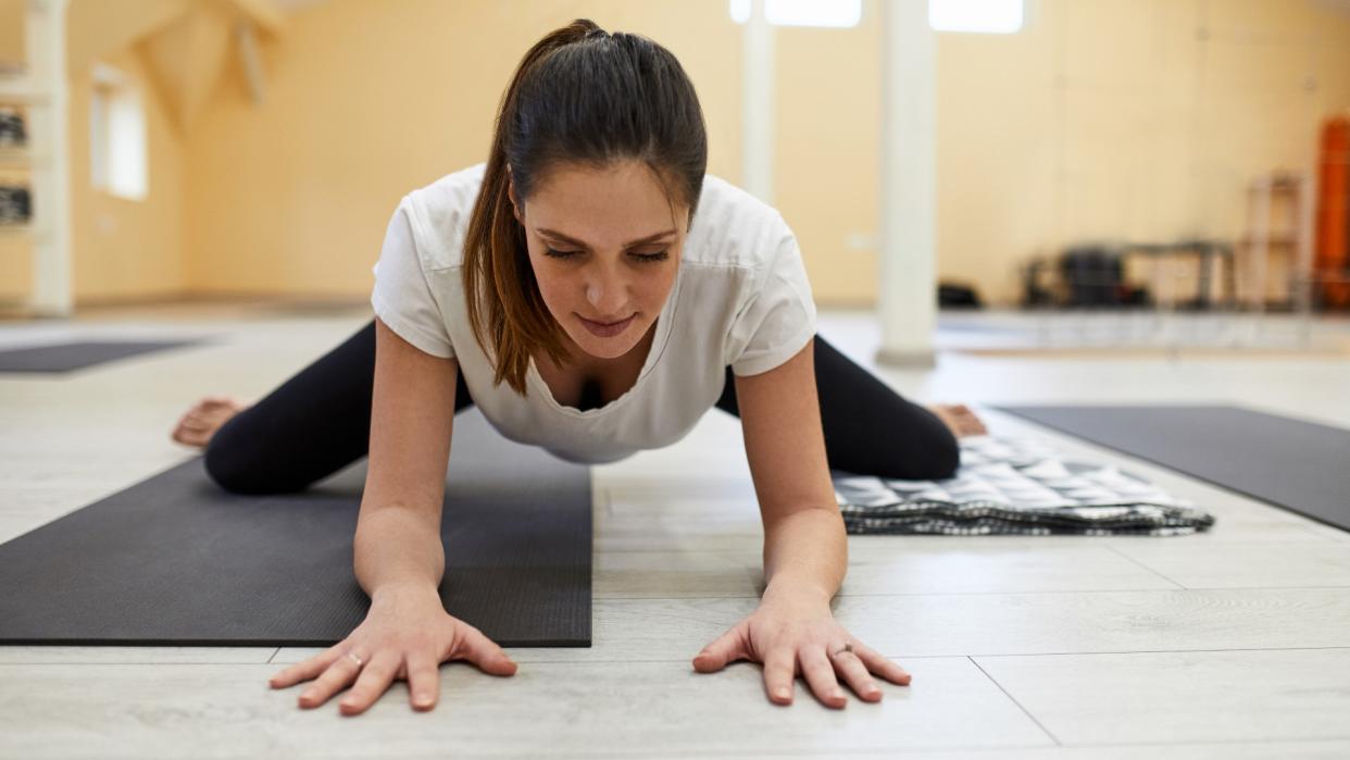  Woman performing frog pose during yoga class on yoga mat. 