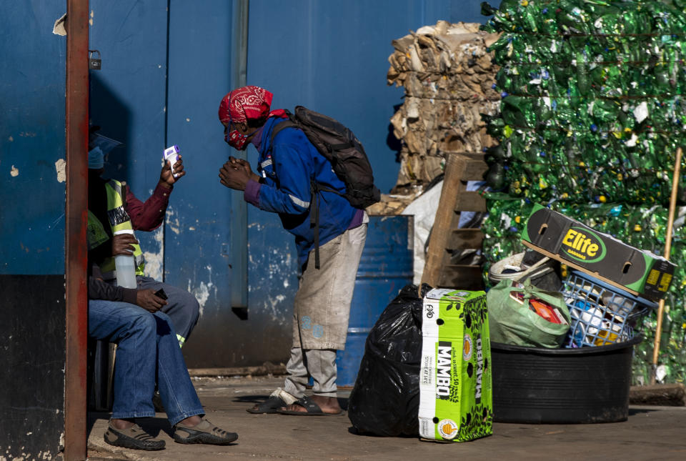 Security personnel measure the temperature of a man before depositing his recycle material for cash at the entrance of a depot in downtown Johannesburg, South Africa, Thursday, May 7, 2020. South Africa begun a phased easing of its strict lockdown measures on May 1, and its confirmed cases of coronavirus continue to increase as more people are being tested. (AP Photo/Themba Hadebe)