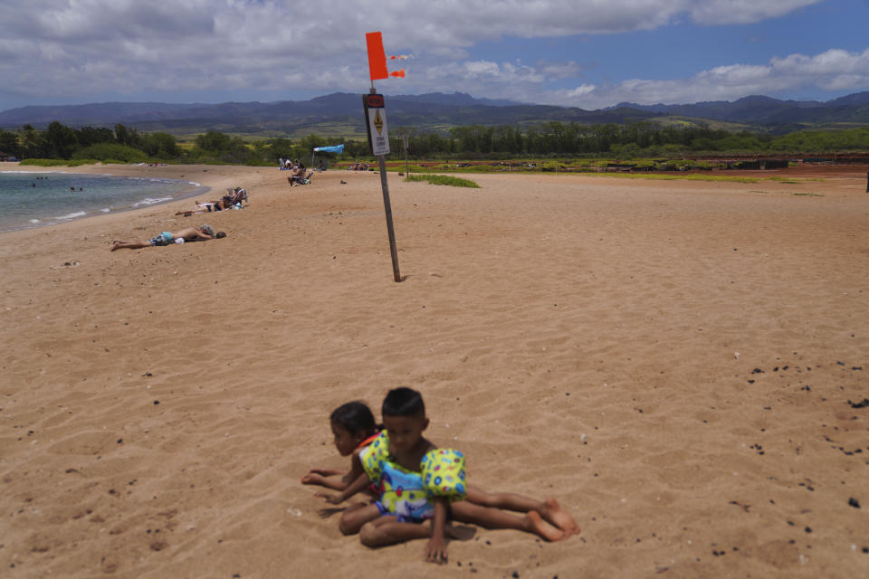 Children play at the Salt Pond Beach Park adjacent to the Hanapepe salt patch on Friday, July 14, 2023, in Hanapepe, Hawaii. Climate change, air pollution and littering by tourists and visitors are all threats to this practice, but the 22 families who continue this tradition are fighting to keep these threats at bay and pass on this sacred practice to future generations. (AP Photo/Jessie Wardarski)