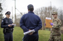 Rhode Island Air National Guard TSgt. William Randall, right, and Westerly police officer Howard Mills talk with New York resident Reha Kocatas who is self-quarantining at his home in Westerly, R.I., Saturday, March 28, 2020. The Rhode Island National Guard started going door to door on Saturday in coastal areas to inform any New Yorkers who may have come to the state that they must self-quarantine for 14 days. (AP Photo/David Goldman)