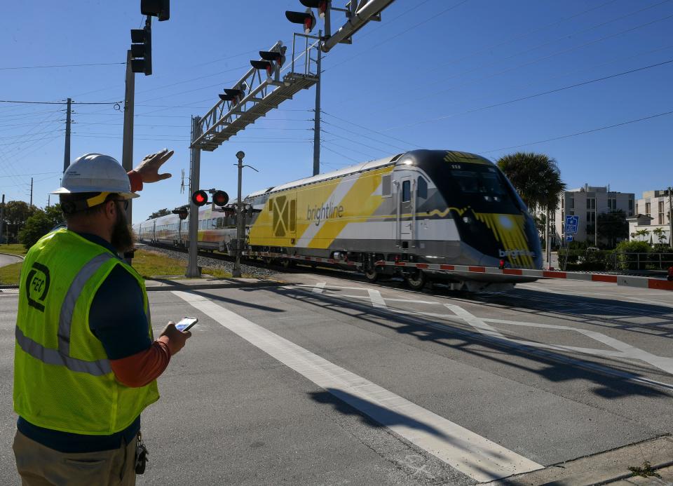 A Florida East Coast Railway crew member stands by as a northbound Brightline qualifying train passes through the westbound traffic lanes of S.R. 60 at Commerce Avenue on Jan. 18, 2022, in downtown Vero Beach.