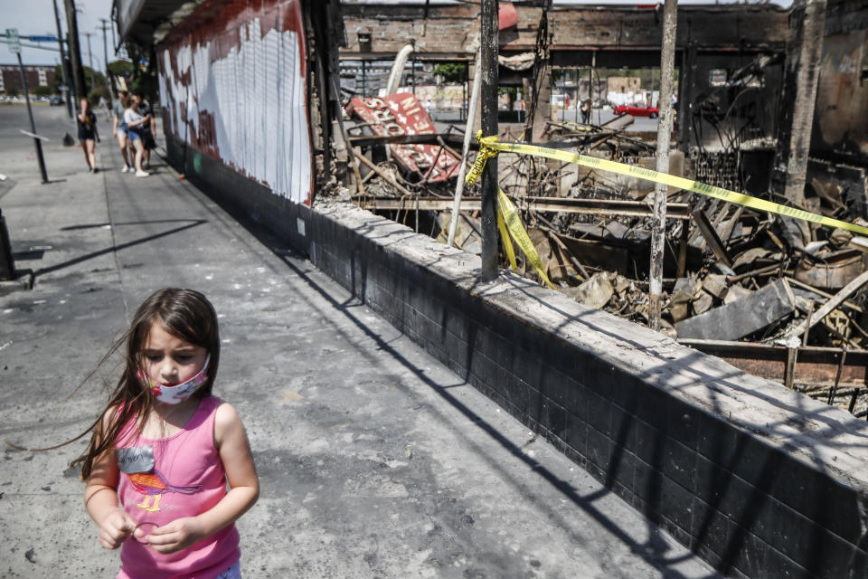 FILE - In this June 2, 2020, file photo, Gretchen Kolden, 6, passes the burned ruins of Minnehaha Liquor store near the Minneapolis 3rd Police Precinct that was destroyed during protests the previous week, in Minneapolis. Protests continued following the death of George Floyd, who died after being restrained by Minneapolis police officers on Memorial Day. (AP Photo/John Minchillo, File)