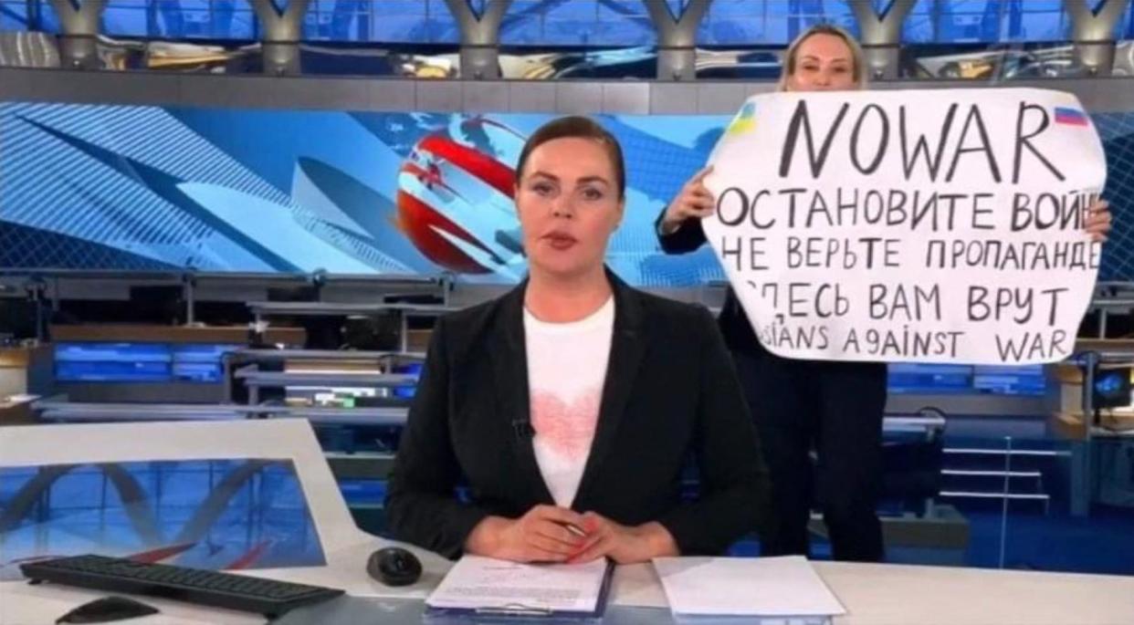 This screenshot taken on March 15, 2022, shows Russian Channel One editor Marina Ovsyannikova holding a poster reading "Stop the war. Don't believe the propaganda. Here they are lying to you," during on-air TV studio by news anchor Yekaterina Andreyev , Russia's most-watched evening news broadcast, in Moscow on March 14, 2022.