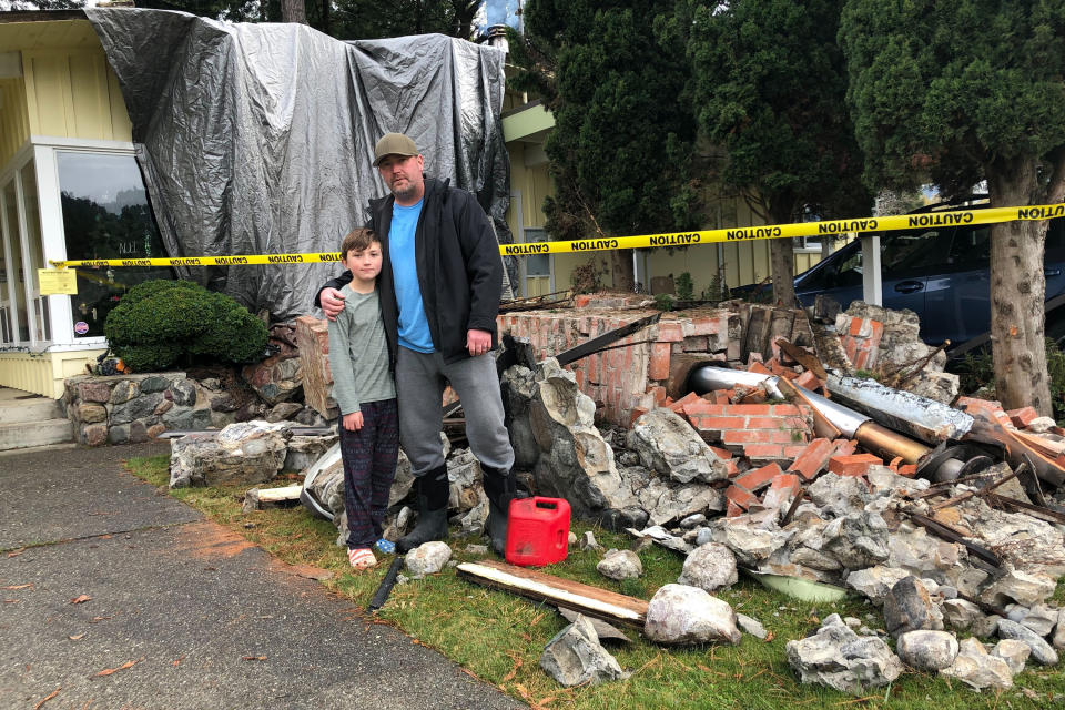 Chad Sovereign and his son, Jaxon, stand in from of their earthquake damaged home in Rio Dell, Calif., Tuesday, Dec. 20, 2022. Chad Sovereign said he grabbed his son and told him he moved him when the quake started. "It felt like the end of the world," Sovereign said. (AP Photo/Adam Beam)