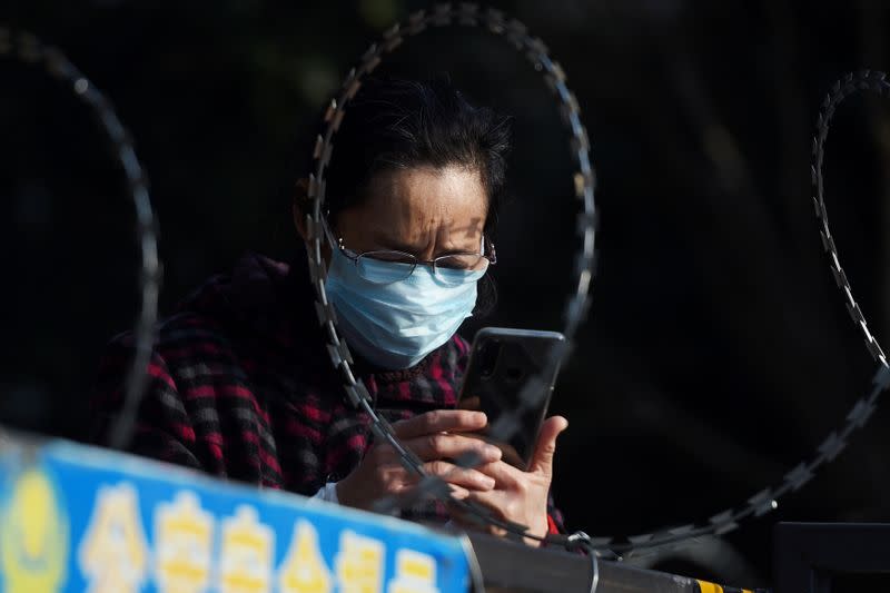 FILE PHOTO: A woman uses her mobile phone behind barbed wire at an entrance of a residential compound in Wuhan