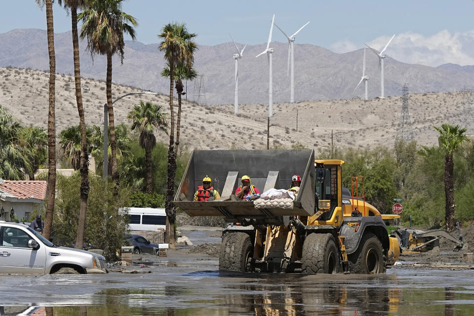 Firefighters use a skip loader to rescue people from an assisted living center after the street was flooded with mud Monday, Aug. 21, 2023, in Cathedral City, Calif. Forecasters said Tropical Storm Hilary was the first tropical storm to hit Southern California in 84 years, bringing the potential for flash floods, mudslides, isolated tornadoes, high winds and power outages. (AP Photo/Mark J. Terrill)