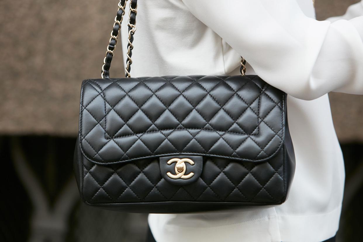 Focus on a black leather Chanel purse hanging on a woman wearing a white jacket during the Milan Fashion Week on september 22, 2016, with a blurred background of the street