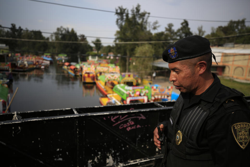 A police officer patrols on a bridge over a canal filled with scores of parked and a handful of occupied trajineras, the colorful passenger boats typically rented by tourists, families, and groups of young people, in Xochimilco, Mexico City, Friday, Sept. 6, 2019. The usually festive Nativitas pier was subdued and largely empty Friday afternoon, with some boat operators and vendors estimating that business was down by 80% on the first weekend following the drowning death of a youth that was captured on cellphone video and seen widely in Mexico. Borough officials stood on the pier to inform visitors of new regulations that went into effect Friday limiting the consumption of alcohol, prohibiting the use of speakers and instructing visitors to remain seated.(AP Photo/Rebecca Blackwell)