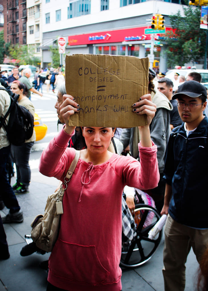 A woman holding a sign that reads, "College Degree = Unemployment. Thanks Wall Street"