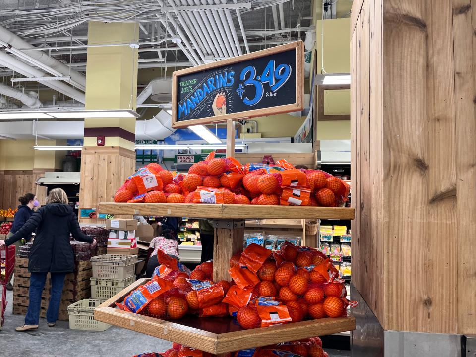 Bags of mandarin oranges on wooden display shelves with a chalkboard sign above them at Trader Joe's