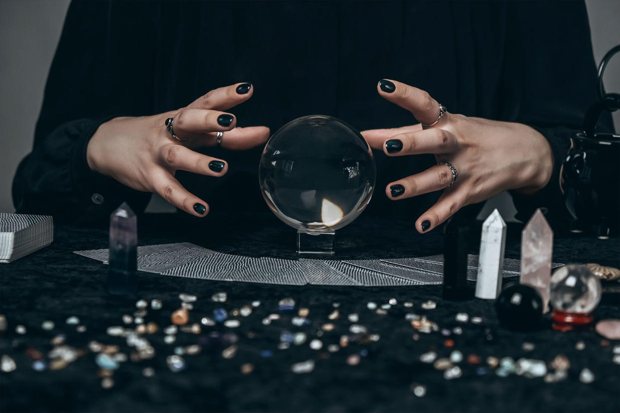 The hands of a young woman conjure over a transparent sphere surrounded by tarot cards, gems and other decor Getty Images/Olena Ruban