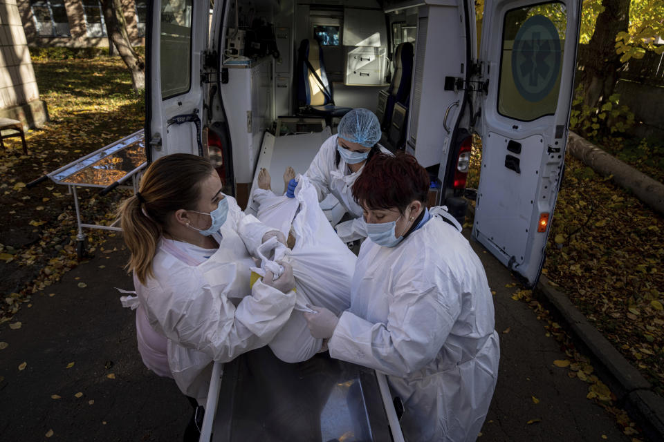 Medical staff members load a body of a patient who died of coronavirus at the morgue of the city hospital 1 in Rivne, Ukraine, Friday, Oct. 22, 2021. In Rivne, 300 kilometers (190 miles) west of Kyiv, the city hospital is swamped with COVID-19 patients and doctors say the situation is worse than during the wave of infections early in the pandemic that severely strained the health system. Ukraine's coronavirus infections and deaths reached all-time highs for a second straight day Friday, in a growing challenge for the country with one of Europe's lowest shares of vaccinated people. (AP Photo/Evgeniy Maloletka)