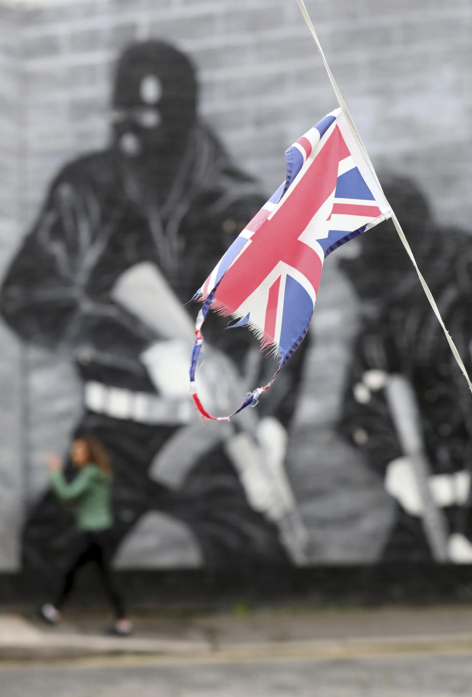 In this Tuesday, Oct. 15, 2019 photo a Union flag flutters in the shadow of a Loyalist mural from the Ulster Volunteer Force in East Belfast, Northern Ireland. (AP Photo/Peter Morrison)