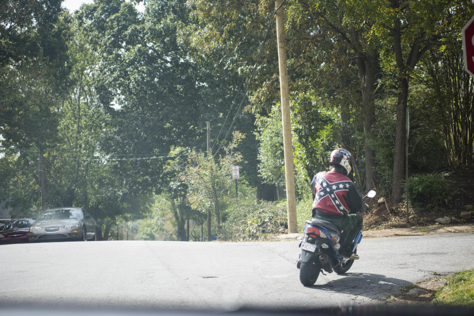 A person&nbsp;wearing a jacket decorated with&nbsp;a Confederate flag passes by on a moped in Asheville.