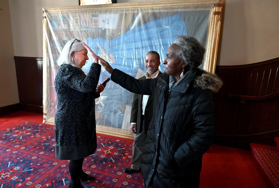 Kathleen Gagne, Mechanics Hall executive director, left, high-fives Gloria D. Hall, co-chair of the Portrait Project, as James Goldsberry looks on after workers managed to get the painting into the building.