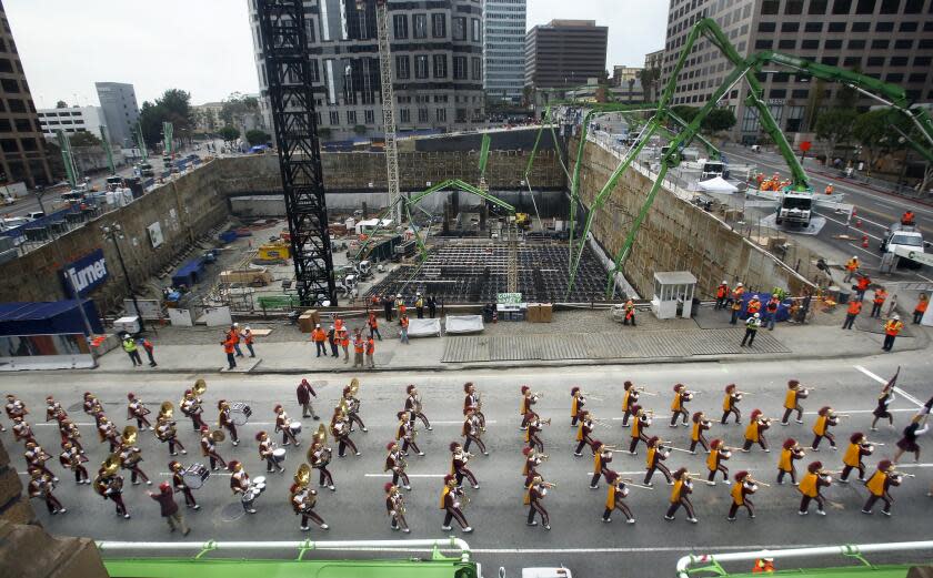 LOS ANGELES, CA-JANUARY 15, 2014: The USC marching band leads a parade on Figueroa St. in Downtown Los Angeles beside the Wilshire Grand Project, seen in background on February 15, 2014. The parade kicked what is being billed as the world's largest continuous concrete pour, expected to last nearly 20 hours. requiring 2100 truck loads delivering 21,200 cubic yards of concrete, weighing 82 million pounds. The 73 story, 1100 foot tall Wilshire Grand Center will be the tallest structure west of the Mississippi River, its developers say, when its 160 foot spire is included. (Photo by Mel Melcon/Los Angeles Times via Getty Images)