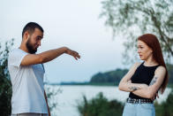 Man pointing finger at a woman with crossed arms in an outdoor setting