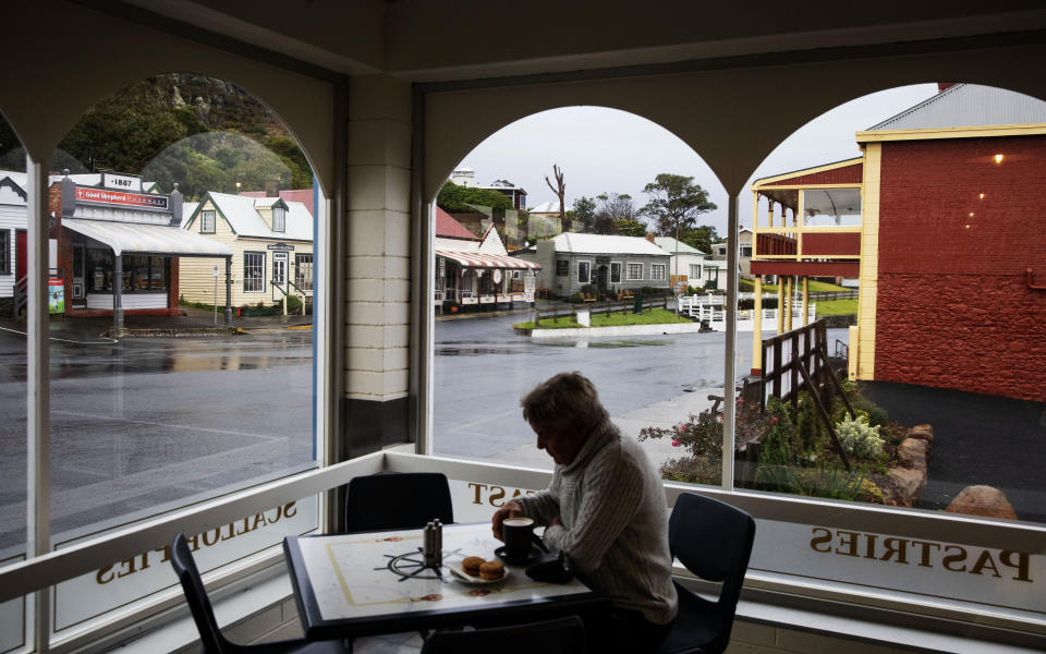 Shops line a street in the town of Stanley as a patron sips a cup of coffee in Tasmania, Australia, Tuesday, July 23, 2019. Like America's Appalachia, Tasmania is the country's epicenter for opioids. It has the nation's highest rate of opioid packs sold per person _ 2.7 packs each. One region has the highest number of government-subsidized opioid prescriptions in Australia: more than 110,000 for every 100,000 people. (AP Photo/David Goldman)