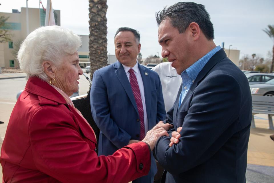 A resident, left, chats with Rep. Pete Aguilar, outdoors, as a man nearby looks on