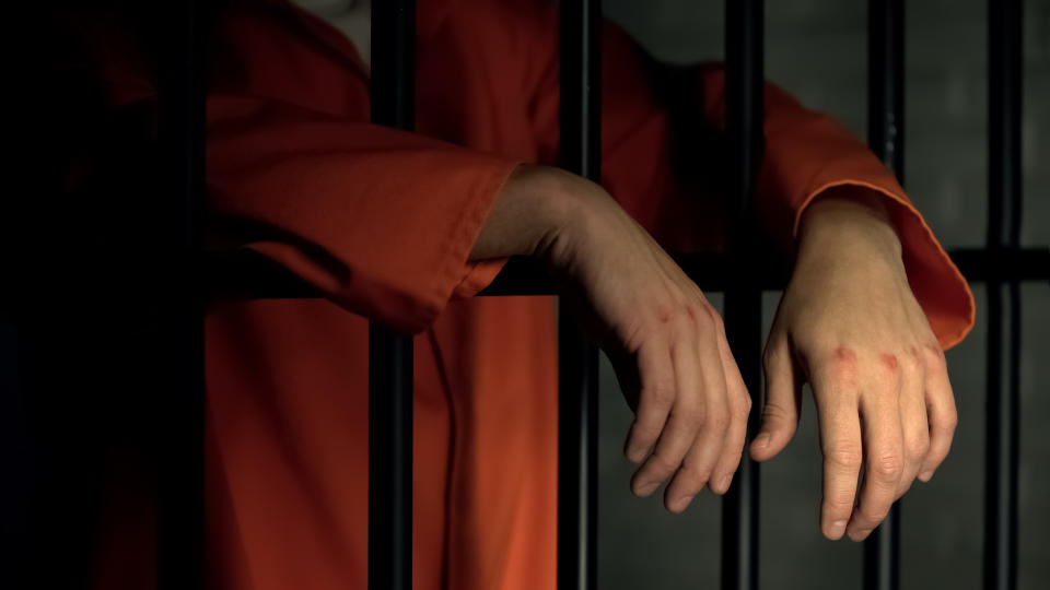 A man's hands leaning out of a prison cell