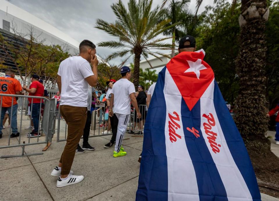 MIAMI, FL- March 19, 2023 - A man wearing a Cuban flag bearing the slogan of Patria y Vida walks towards the entrance of loanDepot Park prior to the baseball game between Cuba and the United States.