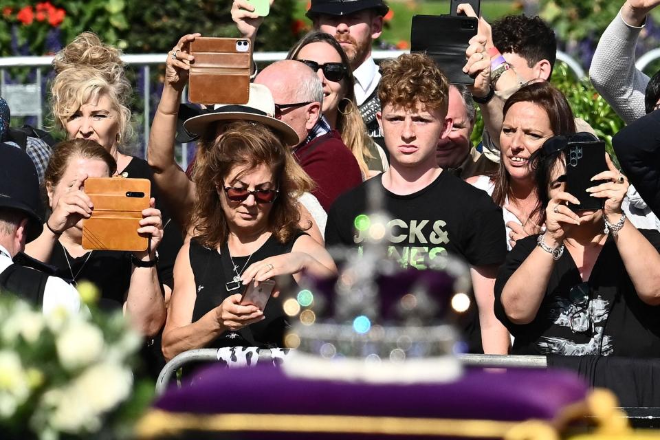 Members of the public watch as the coffin of Queen Elizabeth II, adorned with a Royal Standard and the Imperial State Crown is pulled by a Gun Carriage of The King's Troop Royal Horse Artillery, during a procession from Buckingham Palace to the Palace of Westminster, in London on September 14, 2022.