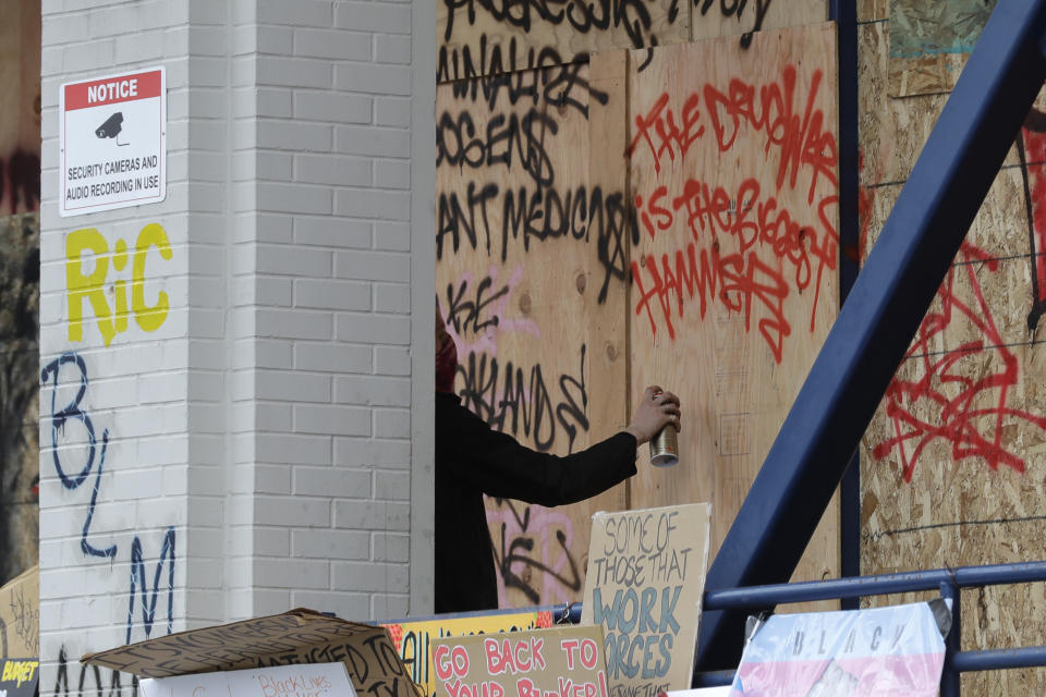 A person sprays graffiti on the Seattle Police East Precinct building, Saturday, June 20, 2020, inside what has been named the Capitol Hill Occupied Protest zone in Seattle. A pre-dawn shooting Saturday near the area left one person dead and critically injured another person, authorities said Saturday. The area has been occupied by protesters after Seattle Police pulled back from several blocks of the city's Capitol Hill neighborhood. (AP Photo/Ted S. Warren)