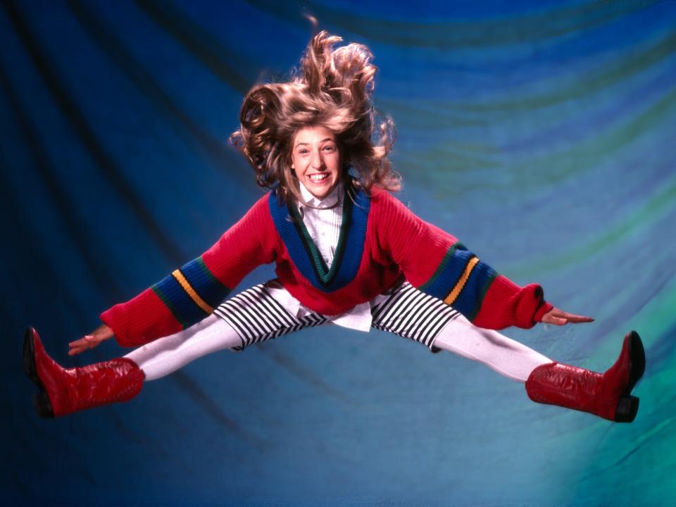 Mayim Bialik jumps into the air doing a split as Blossom.