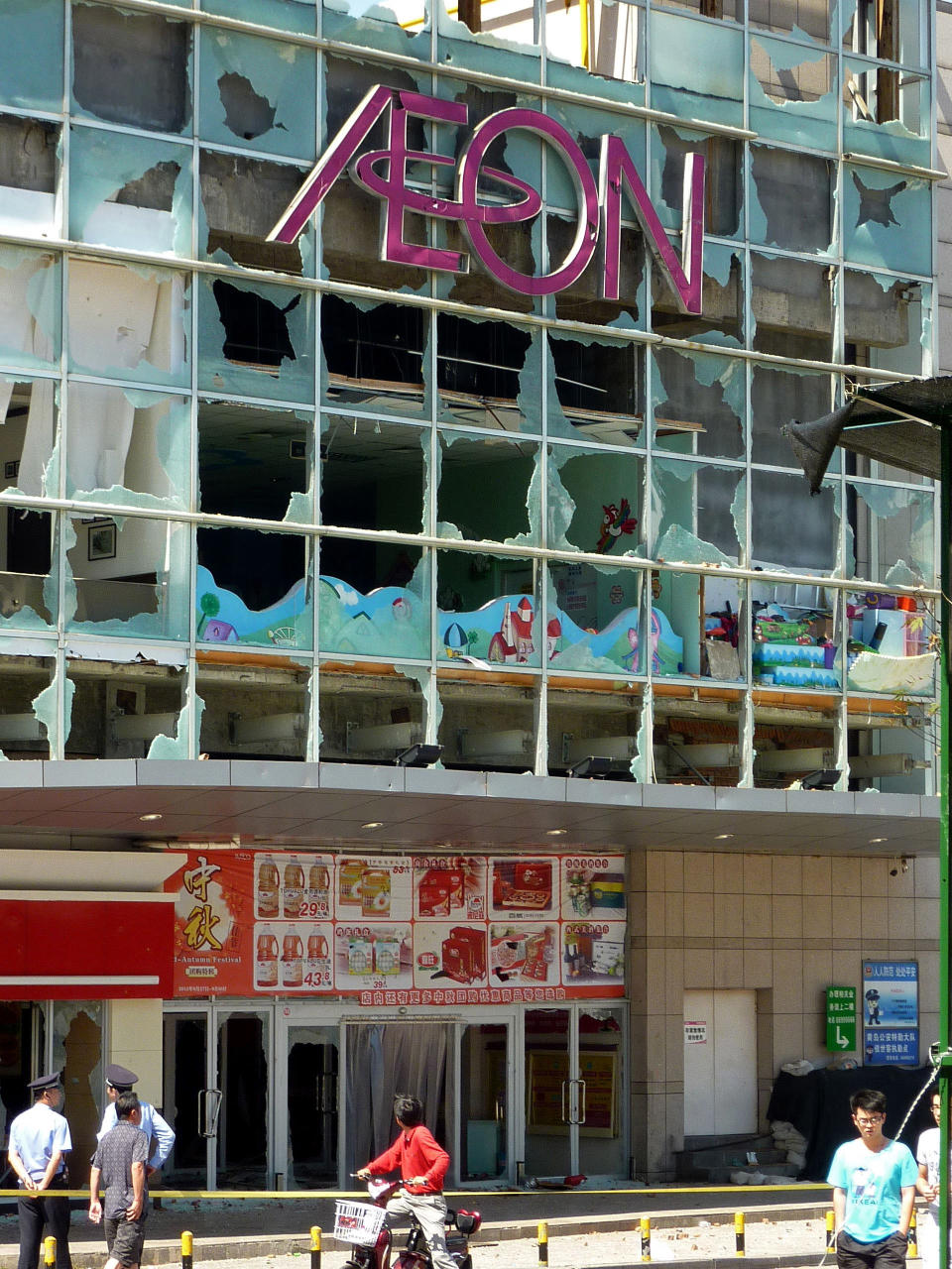 A motorcyclist looks at the damaged facade of an Aeon store in Qingdao, Shandong Province, China, Sunday, Sept. 16, 2012 after demonstrators burst in and destroyed facilities of the Japanese supermarket Saturday. Anti-Japan passions grew more heated this past week in China after Japan's government purchased the contested East China Sea islands - called Diaoyu in China and Senkaku in Japan - from their private Japanese owners. (AP Photo/Kyodo News) JAPAN OUT, MANDATORY CREDIT, NO LICENSING IN CHINA, HONG KONG, JAPAN, SOUTH KOREA AND FRANCE