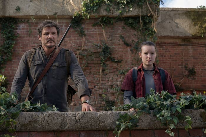 Pedro Pascal and Bella Ramsay stand by a wall in a scene from The Last of Us